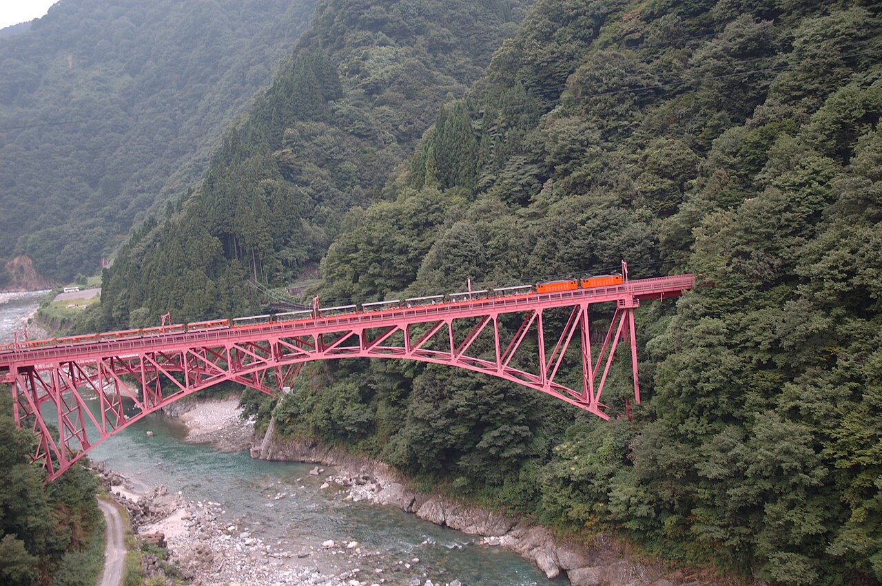 A Kurobe Gorge Railway sightseeing train crossing the red Shin-Yamabiko bridge above the gorge
